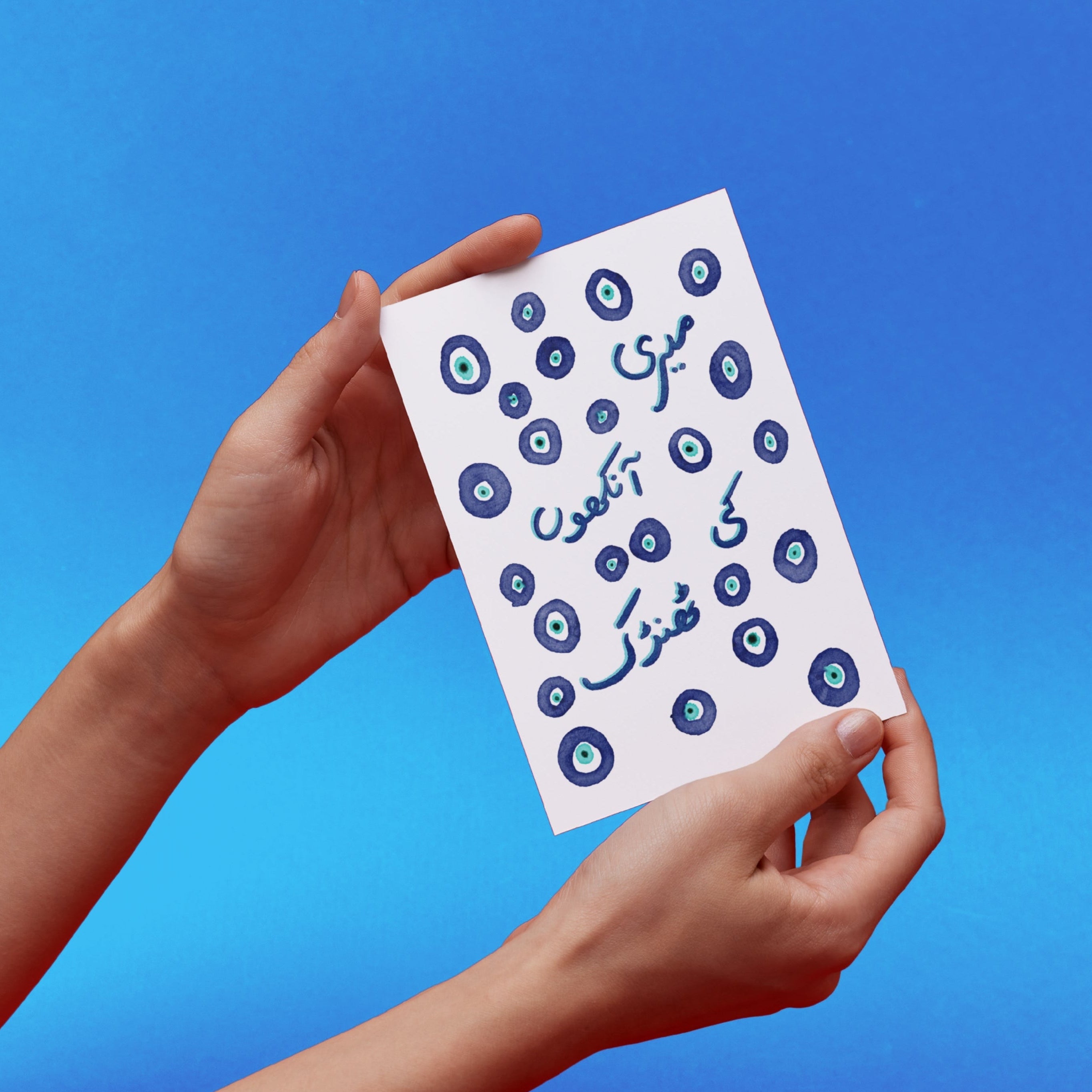 Hands holding a card with Urdu text and blue Turkish eye illustrations