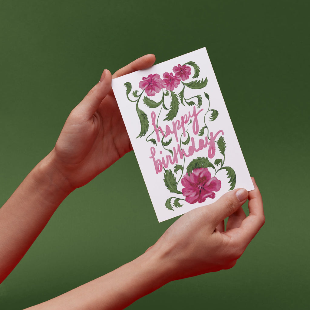 Hands holding a 'Happy Birthday' card with original pink floral designs 