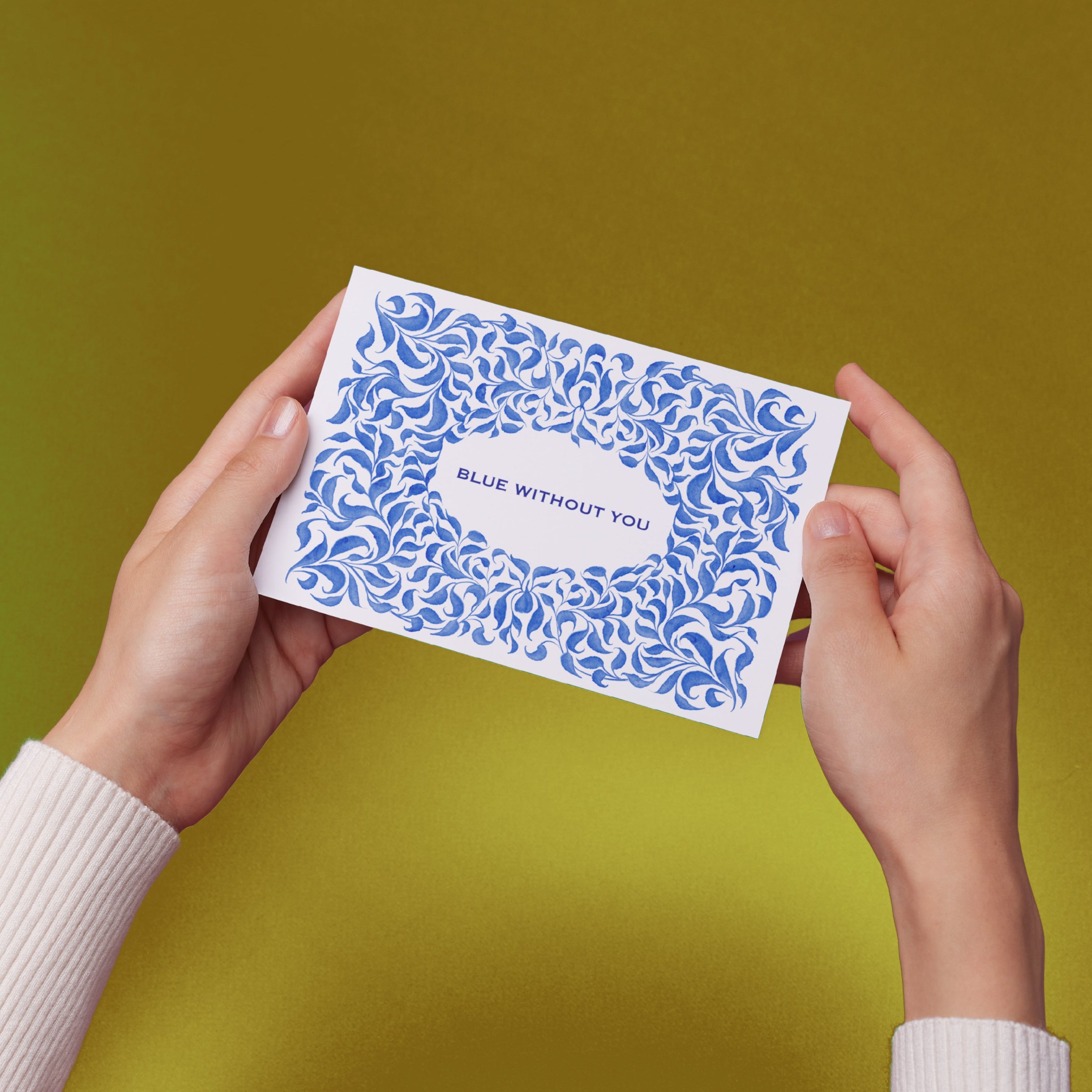 Hands holding a card with original blue vines illustration and text "Blue Without You" against a yellow background