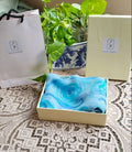 Folded chiffon fabric with hand painted blue swirls, displayed in a box next to Atelier Ambereen packaging 