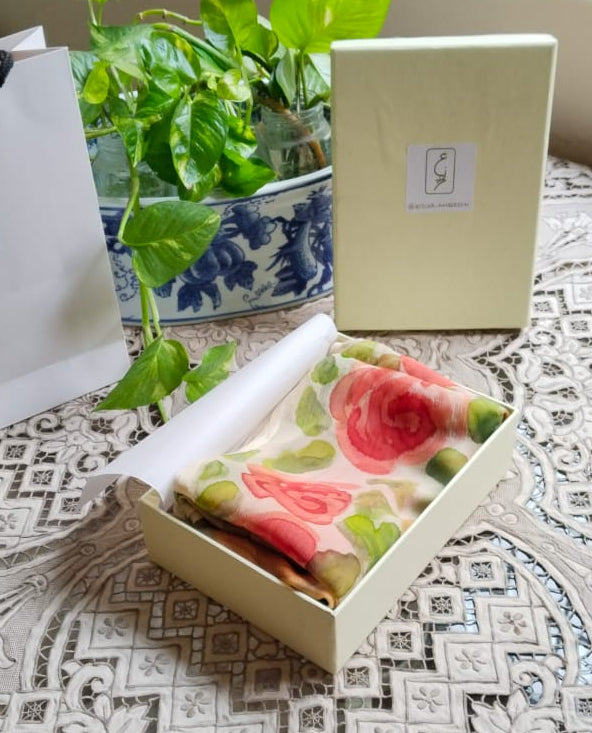 A cream-colored gift box containing a folded hand painted floral-patterned chiffon fabric item, displayed in Atelier Ambereen 