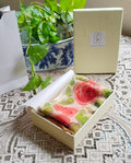 A cream-colored gift box containing a folded hand painted floral-patterned chiffon fabric item, displayed in Atelier Ambereen 