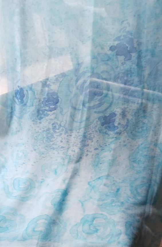 A light blue sheer fabric draped over a surface. The fabric features a subtle watercolor-style floral pattern in various shades of blue.