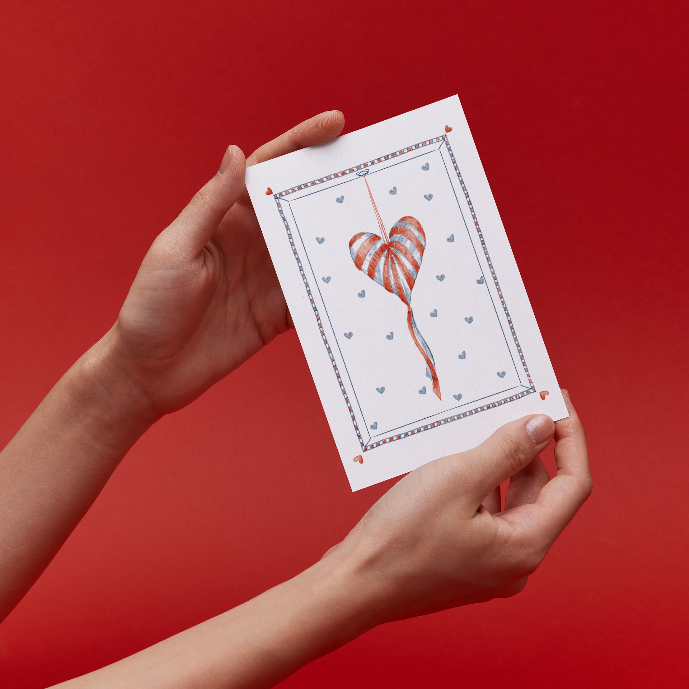 Hands holding a card with an original illustration of a Heart shaped striped pinata against a backdrop of smaller hearts