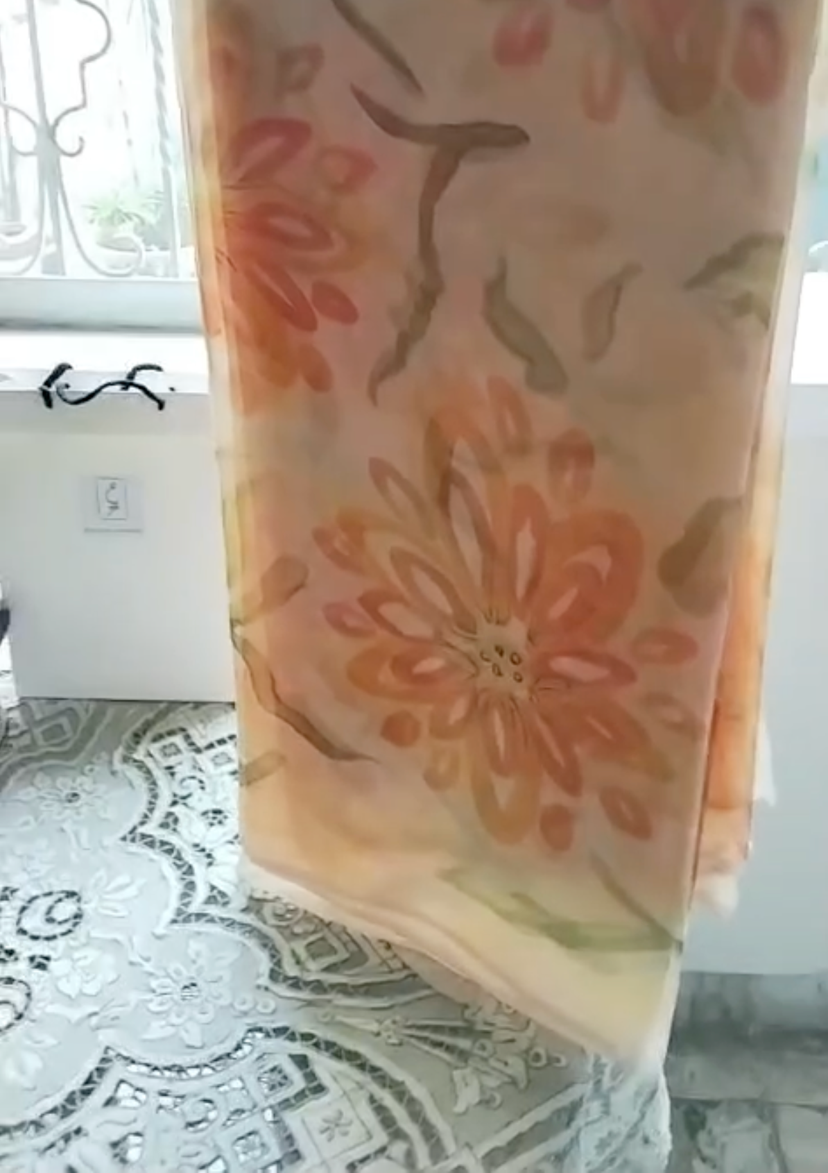 Hand Painted Pure Chinese Crinkle Chiffon with yellow and orange flowers and green stems hanging in front of a window