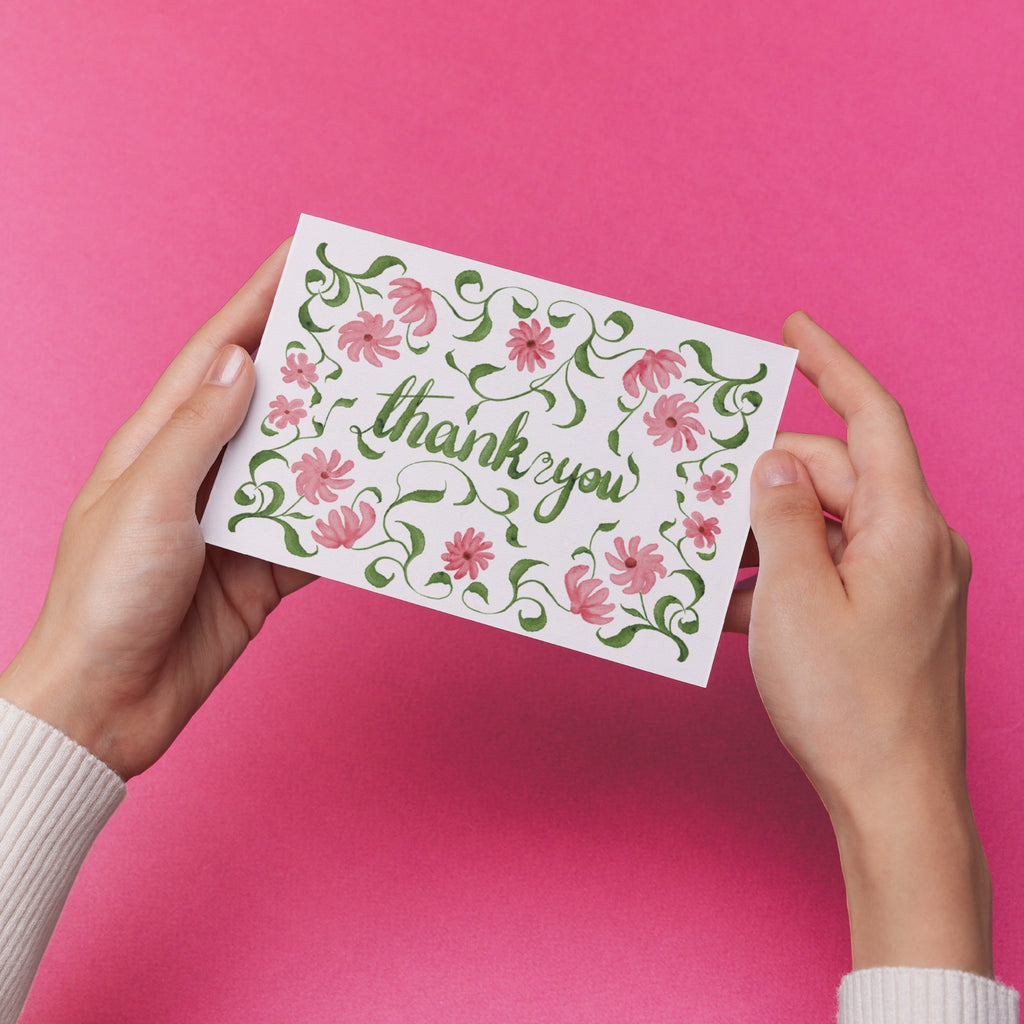 Hands holding a 'thank you' card with original delicate pink floral design